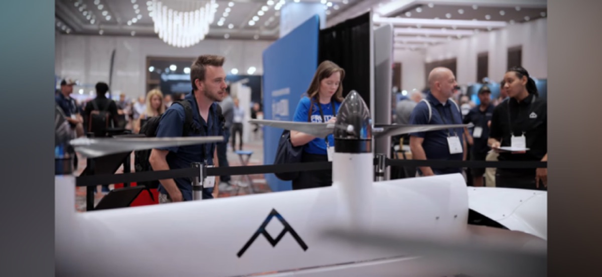 An AIBOT aircraft prototype displayed at an aerospace expo while Lauren speaks with visitors nearby